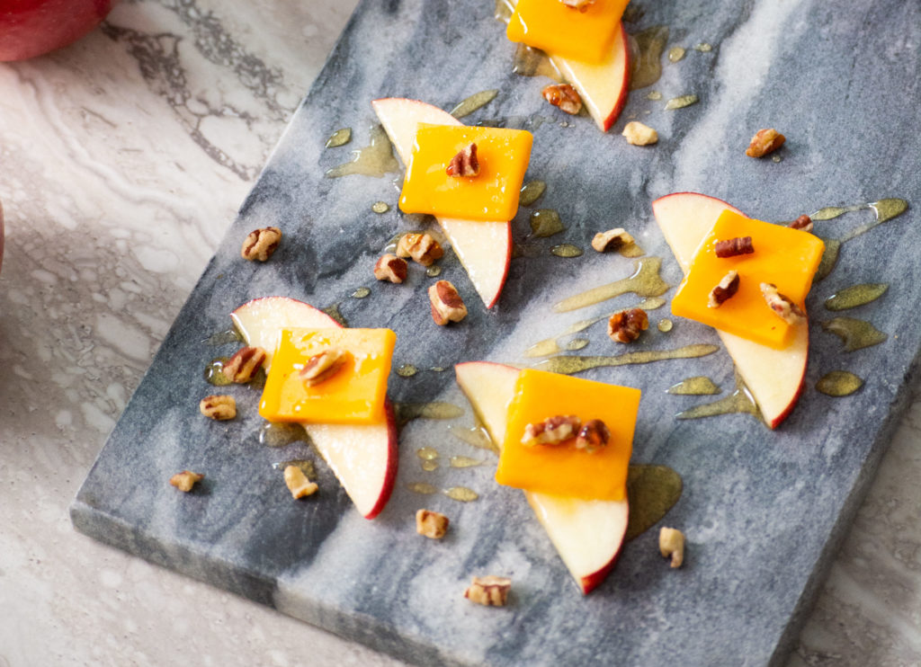 Sliced SweeTango Apples topped with slices of cheddar cheese, chopped pecans and drizzled with honey.